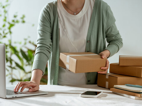 Woman preparing packages for shipping while working on her laptop