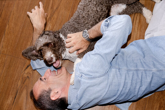 Happy senior man cuddling playful dog while lying on floor at home
