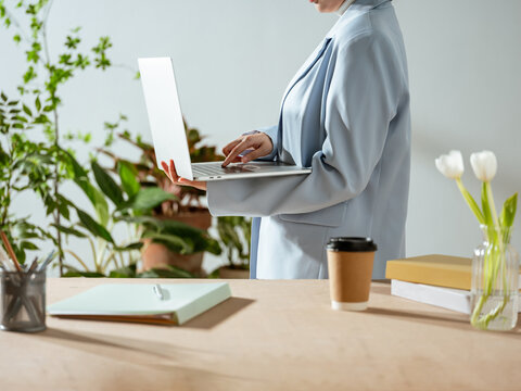 Woman in blue suit using laptop at a desk with plants