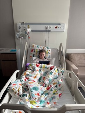Child resting in hospital bed with tablet