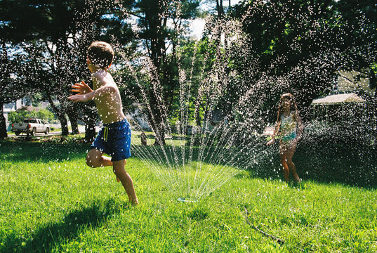 Two children play outside in backyard sprinkler