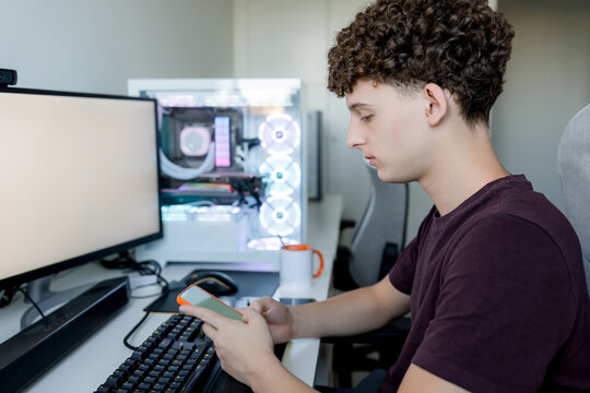 Young man use smartphone at gaming computer desk