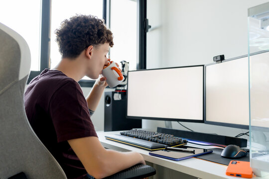 Young man drink coffee at dual monitor computer desk
