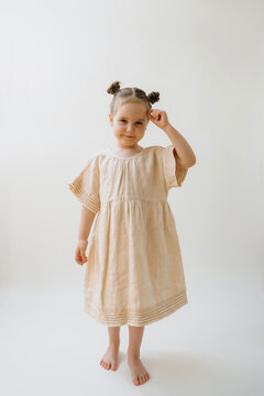 Cute little girl in a beige linen dress on white background