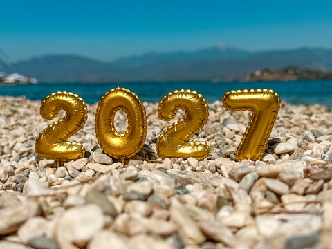 Golden 2027 balloon numbers on a pebble beach at dusk