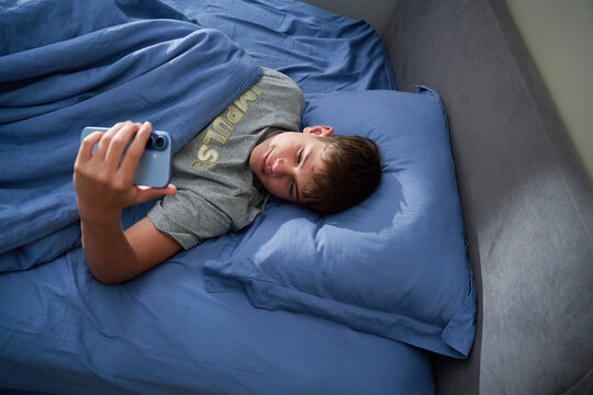 Teen boy lying in bed scrolling smartphone with smile