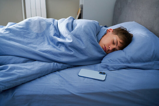 Teen boy sleeping in bed with smartphone lying nearby