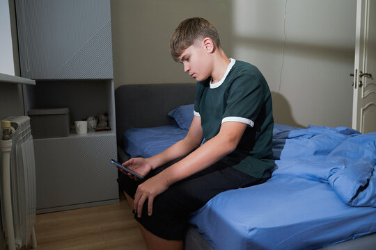 Teen boy sitting on bed looking at smartphone screen