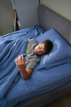 Teen boy lying on back using smartphone in bed