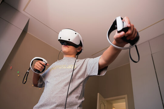 Teen boy playing virtual reality game with VR headset and controllers