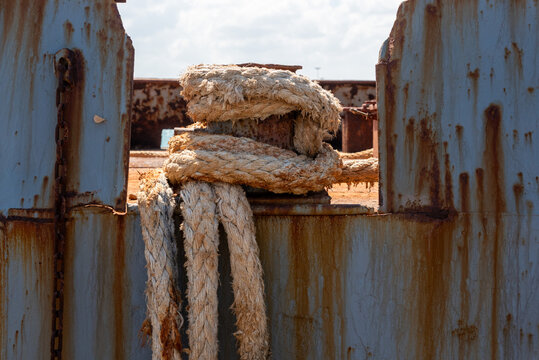 Rusted Mooring Rope Wrapped Around Single Bollard on Grey Ship Hull in Crete