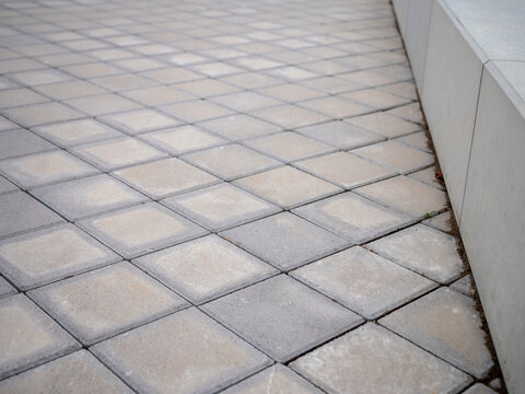 Concrete paving blocks forming a geometric walkway beside a concrete wall. Detail of interlocking pavement suitable for construction, landscaping, hardscape and urban design concepts.