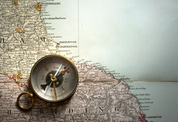 Vintage brass compass on an old England geographic map.  Antique navigation instrument for travel, exploration, geography and discovery concept. Adventure, tourism, cartography and orientation theme. © Tryfonov