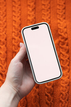 Hand hold smartphone against orange knitted sweater