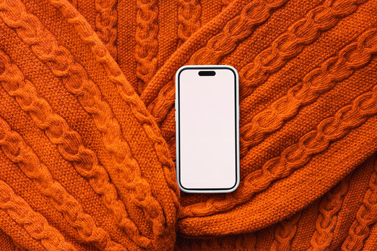 Smartphone on orange cable knit sweater texture