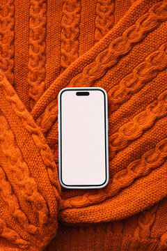 Smartphone on orange cable knit sweater background