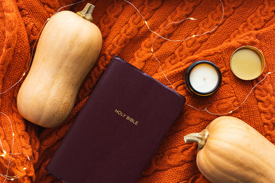 Holy Bible with squash and candle on orange sweater