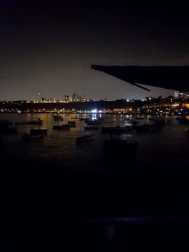 Dark ocean bay at night with silhouetted boats and distant city lights