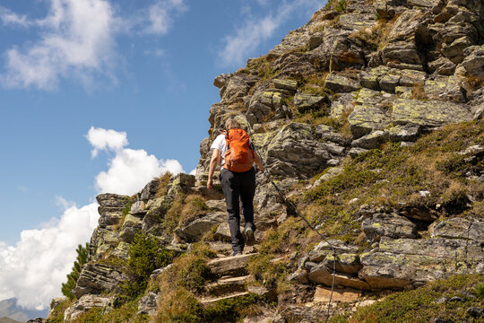 Hiker with orange backpack climbing a rocky mountain trail