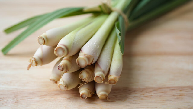 Fresh raw lemongrass stalks tied in a bundle resting on a wooden cutting board table. Essential aromatic Asian culinary herb and aromatherapy ingredient