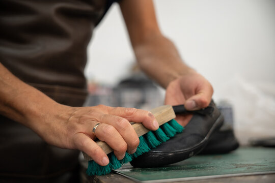 Shoemaker brush polish onto black leather shoe in workshop