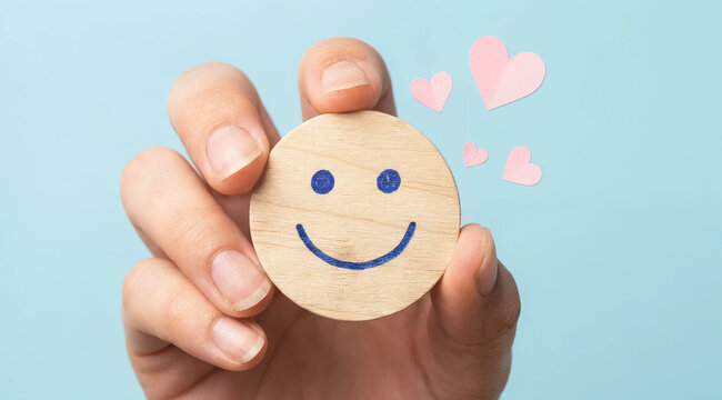 Human hand holding wooden round token with smiley face and pink paper hearts wood token customer satisfaction positive feedback emotional state