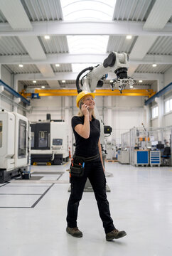 Woman engineer use smartphone beside industrial robot