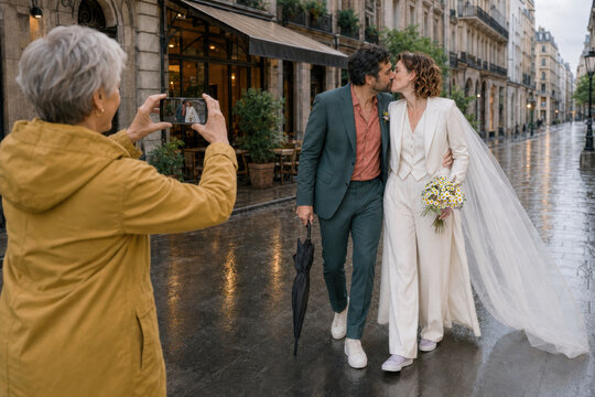 Newlywed couple kiss on rainy city street after wedding