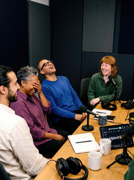 Diverse podcast panel laugh together in recording studio