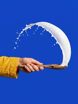 Milk splash over wooden spoon on vivid blue background