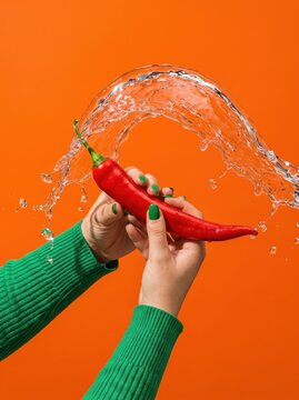 Hand hold red chili pepper beneath water splash