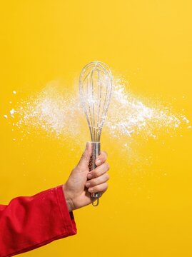 Hand whisk scatter flour against vibrant yellow backdrop