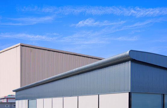 Warehouse building with corrugated metal sheet facade in industrial modern factory area and blue sky background. Perspective side view with copy space