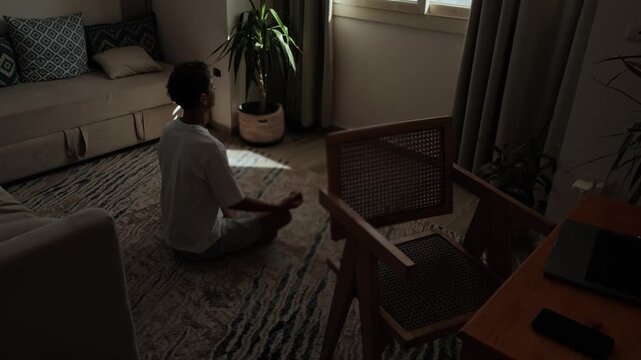 Man practicing mindfulness at home during a work break, sitting quietly between a bedroom and workspace to disconnect from screens, restore mental energy and prepare to return to work