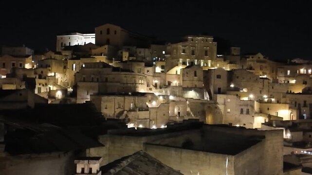 Breathtaking panoramic view of the ancient city of Matera (Sassi di Matera) at night, beautifully illuminated with warm golden lights. UNESCO World Heritage Site in Basilicata, Southern Italy. 4k