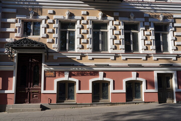 An elegant historic building facade features prominent decorative bossage, large rectangular windows, and a classic carved wooden entrance topped by an ornate wrought iron canopy in Tbilisi, Georgia © Gregory