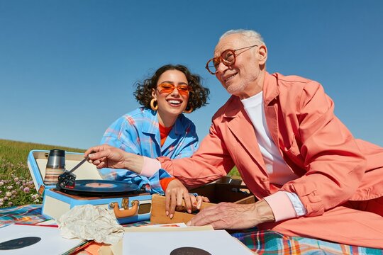 Music and indie culture scene with a grandfather and granddaughter playing a vinyl record in a sunny field for family and generation campaigns