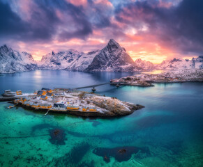 Sakrisoy fishing village with yellow houses in Lofoten islands, Norway. Aerial drone view of snow covered mountains, bridge, turquoise ocean water, sky, clouds and dramatic sunset lighting. Top view © den-belitsky