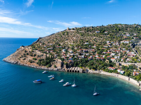 High angle view of Alanya historic peninsula, Tersane shipyard, old shipyard, moored boats and coastal landscape in Antalya, Turkey. Mediterranean blue sea, architecture and sunny blue sky.