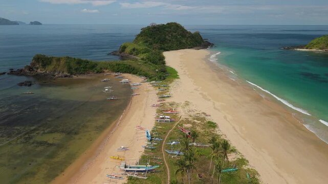 Drone footage over Nacpan and Calitang Twin Beach in El Nido, Palawan, capturing the distinctive shape of the two beaches, white sand shoreline and surrounding tropical landscape.