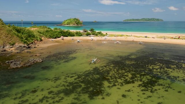 Drone footage over Nacpan and Calitang Twin Beach in El Nido, Palawan, capturing the distinctive shape of the two beaches, white sand shoreline and surrounding tropical landscape.