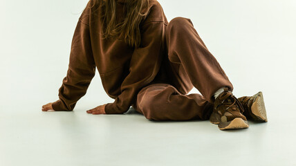 A young person wearing a comfortable brown fleece tracksuit sitting on a bright white background © shine.graphics