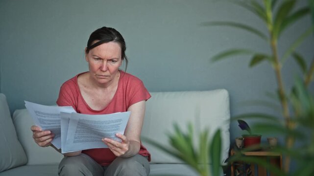 Anxious middle-aged woman reviewing financial paperwork and debt documents outdoors. Concept of budgeting, household expenses, financial difficulties, and money management. 4K.