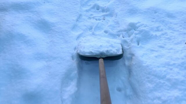 Black plastic snow shovel scooping and pushing thick layer of fresh winter snow from walkway. Man cleaning a backyard path after a heavy blizzard. Active outdoor house care and domestic chore concept.