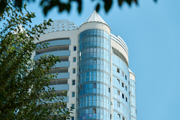Low angle shot showing top floors and distinctive glass corner turrets of a high-rise white and blue residential building rising against clear blue sky © Алексей Филатов