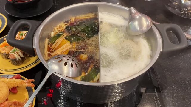 A close-up of a  hot pot meal featuring divided broth, vegetables, meat, and cooking utensils of preparing fresh ingredients in a steaming hot pot shabu, mala, and communal dining.