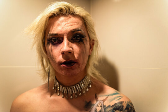 Person with makeup and tattoos, wearing a jeweled choker, indoors.