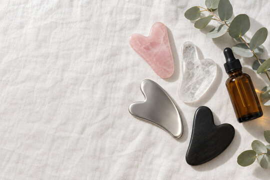Flat lay of gua sha tools in rose quartz, clear quartz, steel and bian stone