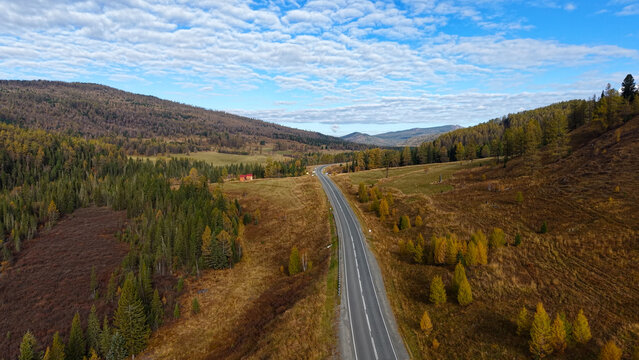 Beautiful aerial panoramic high angle view of an asphalt road heading through a picturesque mountain valley in autumn.