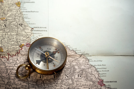 Vintage brass compass on an old England geographic map.  Antique navigation instrument for travel, exploration, geography and discovery concept. Retro compass with directional needle on map.